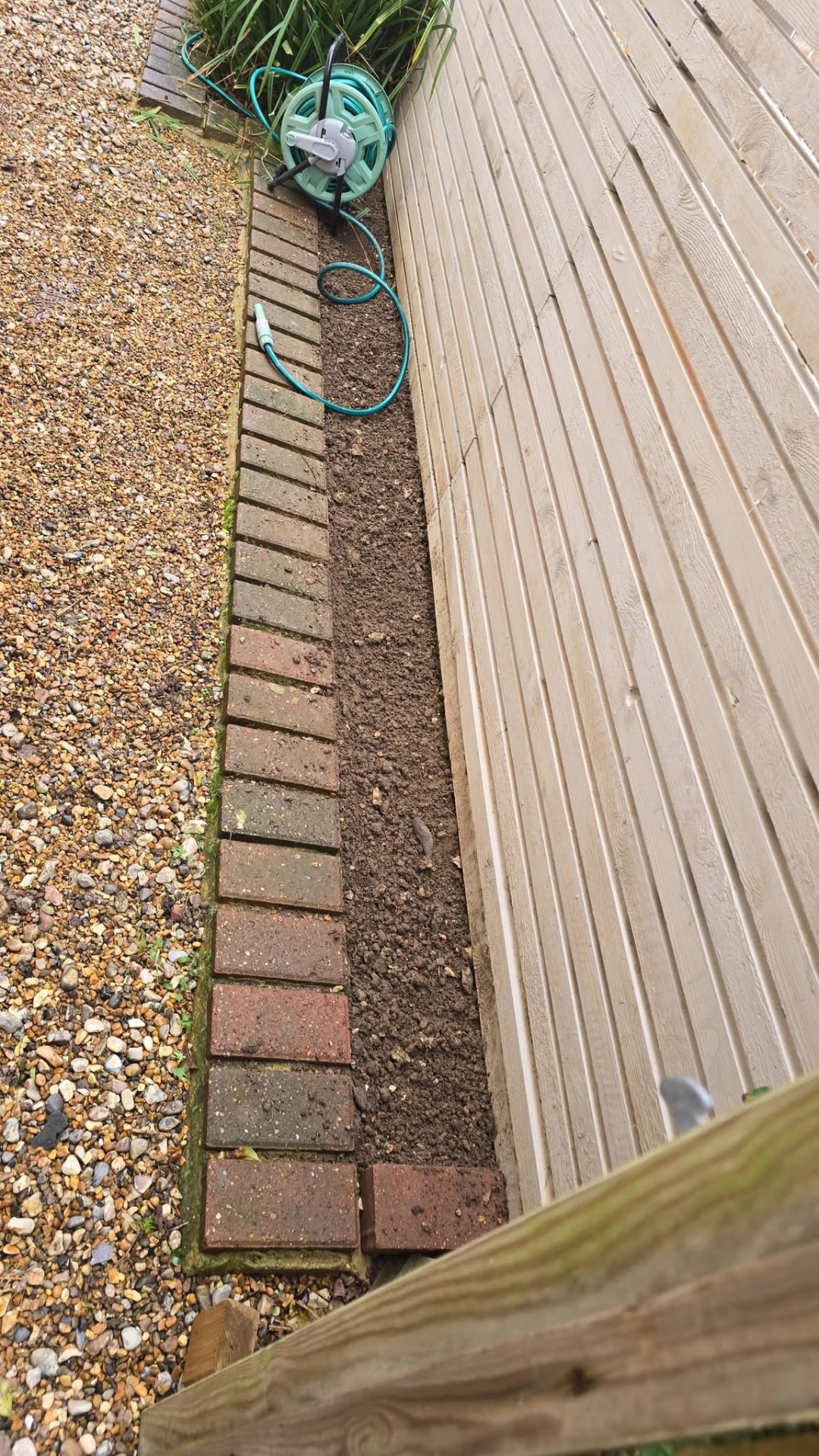 Brick edging installed alongside decking with prepared border soil