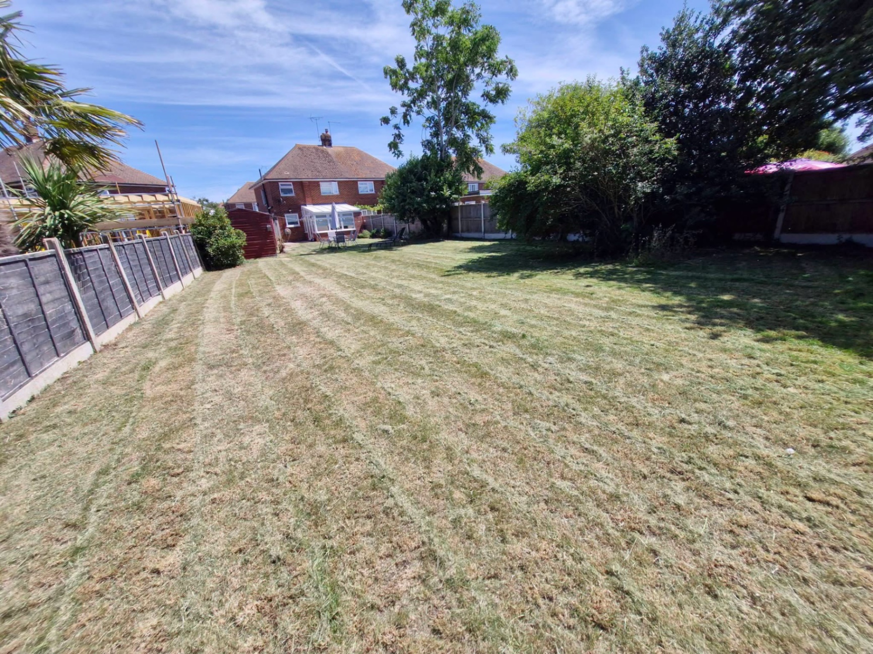 Large rear lawn cut back in summer heat behind semi-detached home