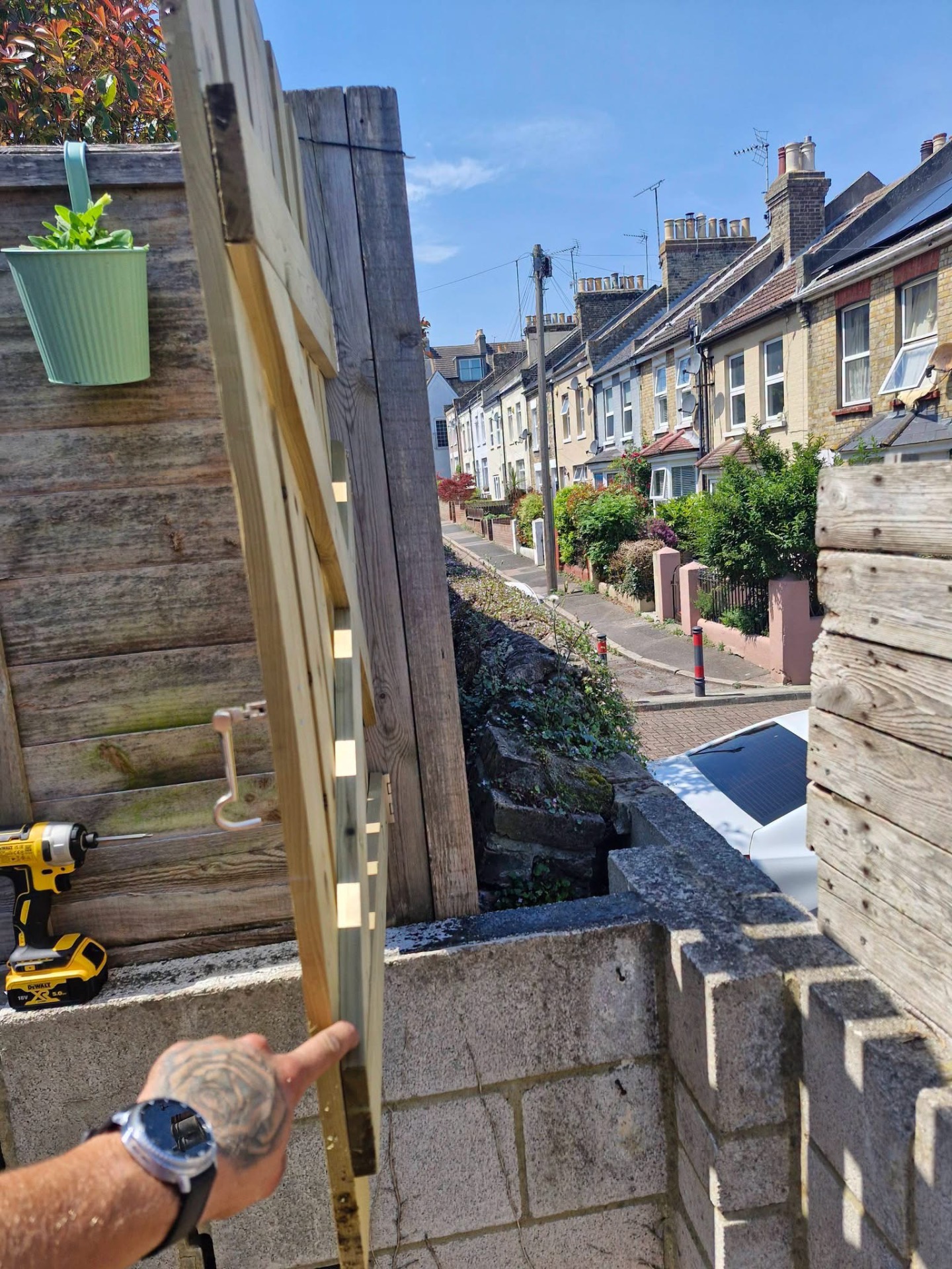 Fitting a new timber side gate with cordless drill on brick wall