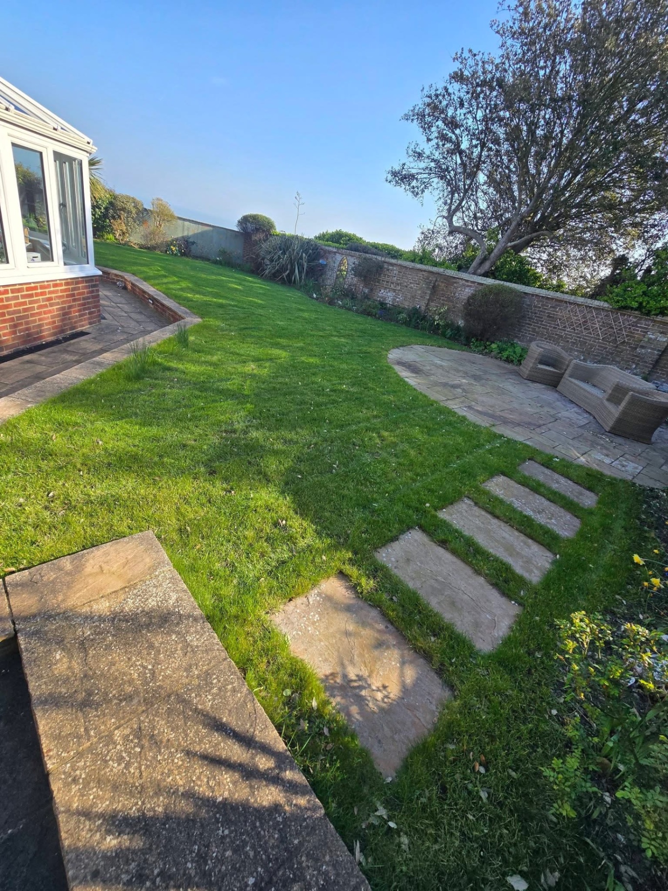 Walled coastal garden with cut lawn, stepping stones and patio seating