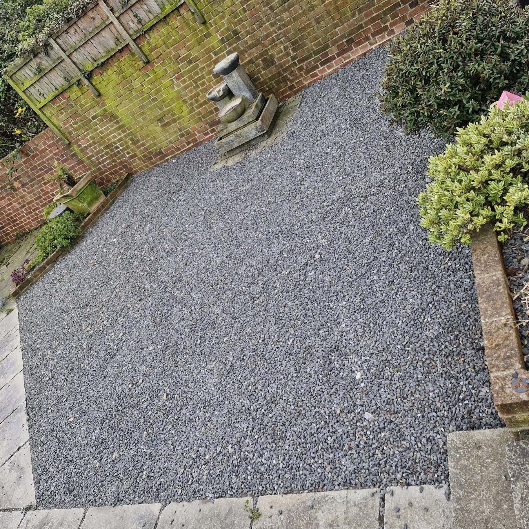 Slate chipping garden with stone water feature against brick wall