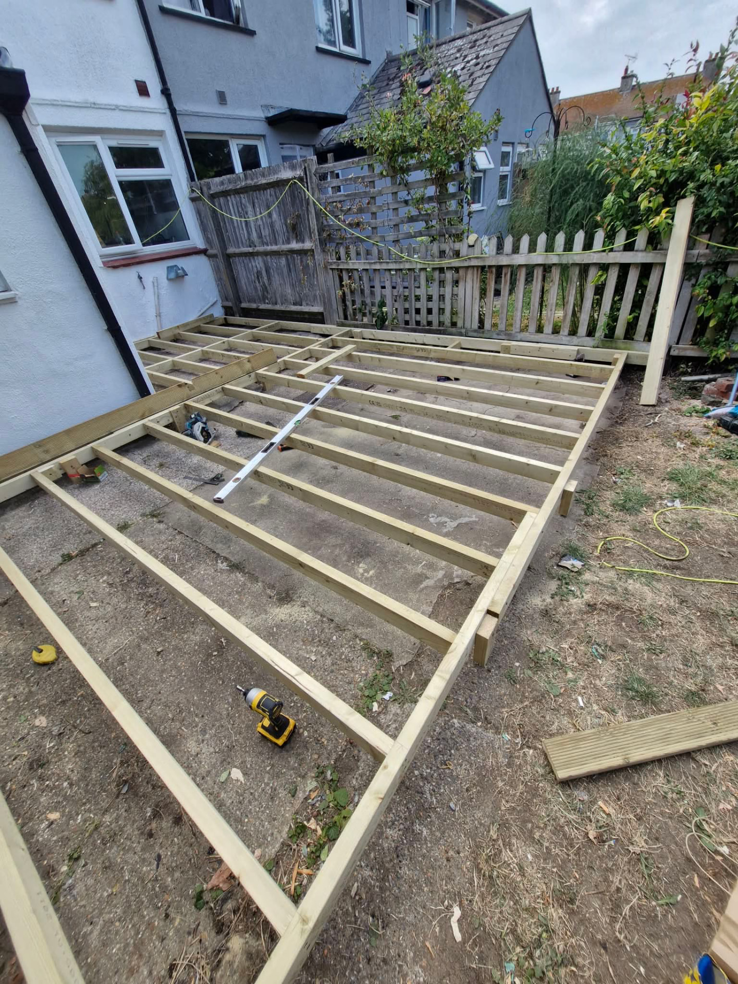 Large decking frame spanning a rear garden beside a picket fence