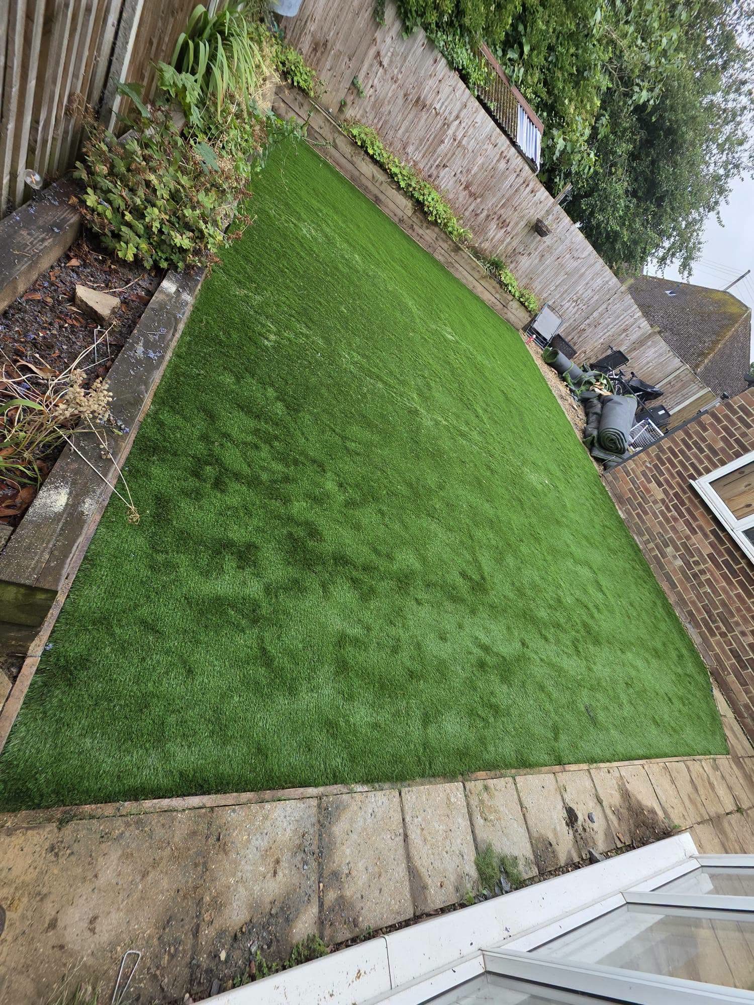 Freshly laid artificial lawn on a long back garden with sleeper edging