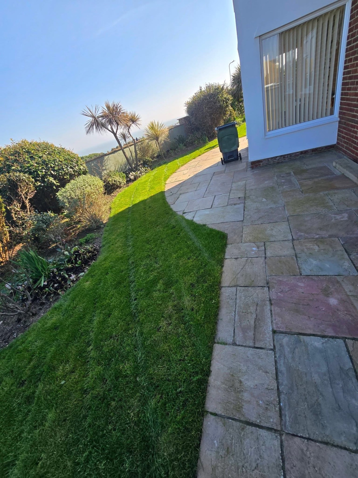 Curved rear lawn freshly cut alongside sandstone patio