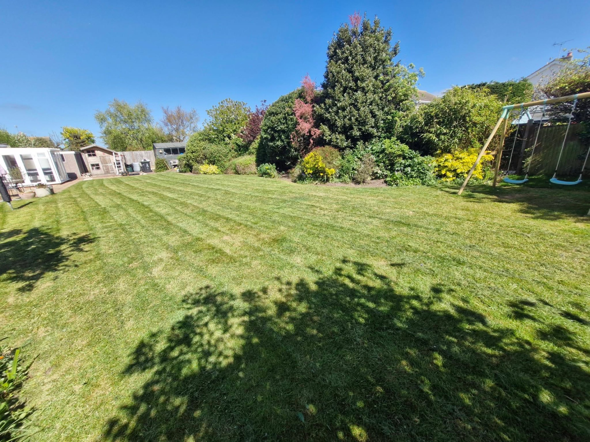 Family back garden lawn cut around swing set and mature borders